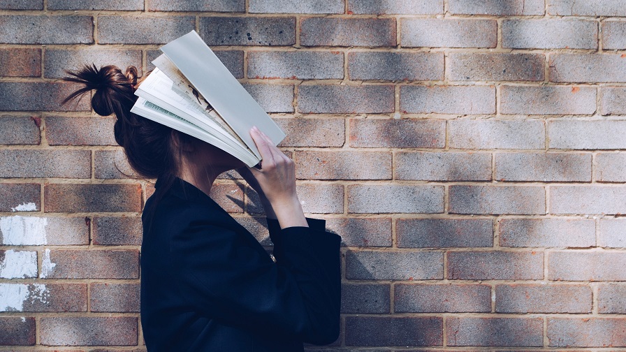 Studentin hält Buch ins Gesicht